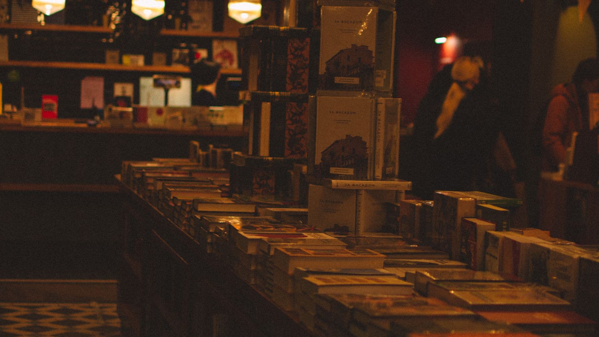 Tables of secondhand books under warm lamps in an evening bookshop