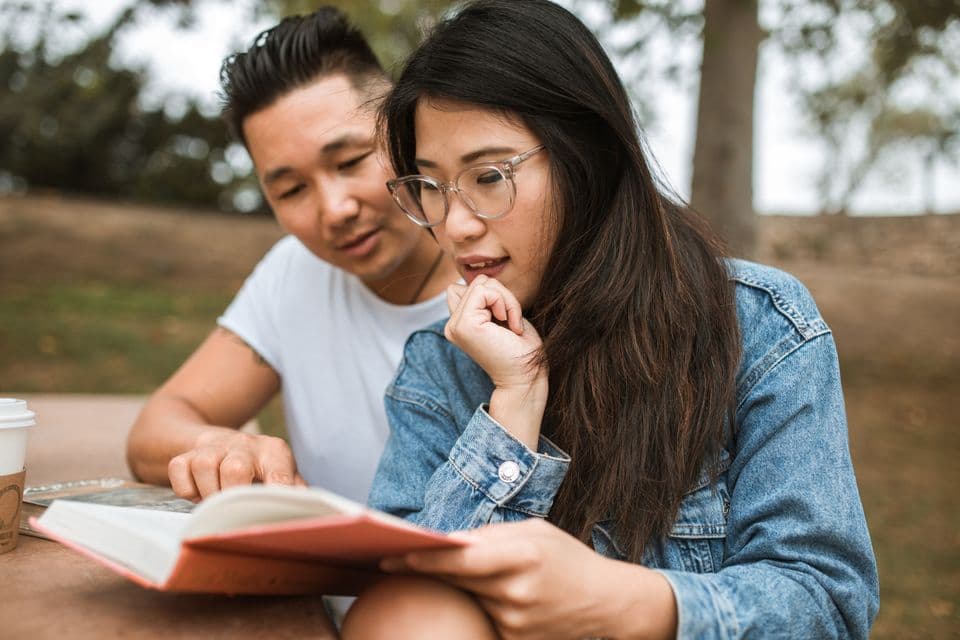 Two neighbors reading one book together at a park table